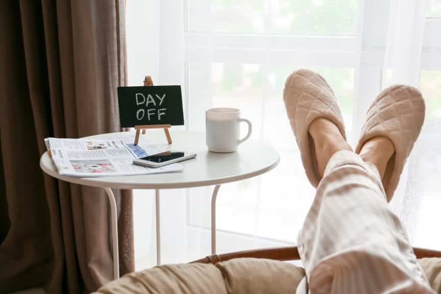 Feet with slippers and coffee table with mug and sign that says day off.