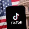 Phone opening TikTok in front of American flag and Capitol Building background