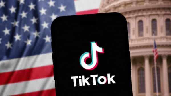 Phone opening TikTok in front of American flag and Capitol Building background