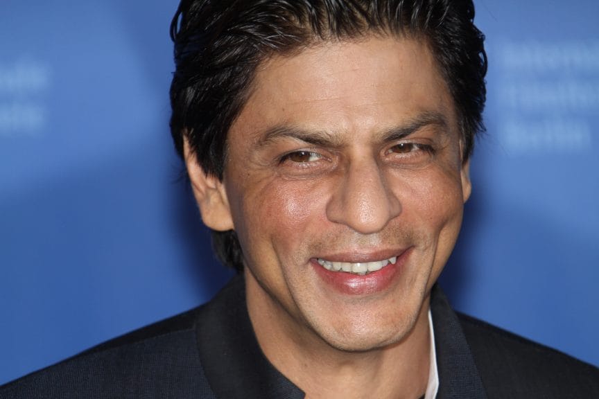 A South Asian man smiling in front of a blue backdrop