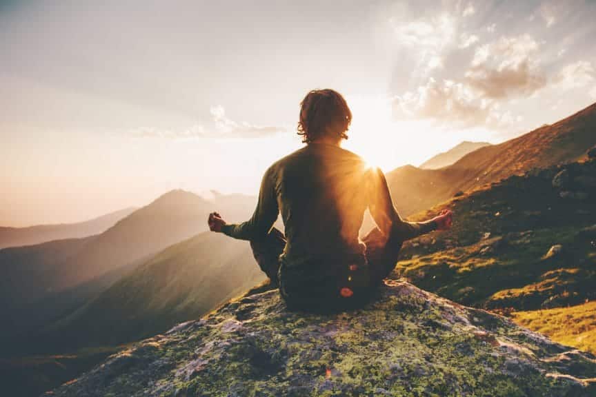 man sitting on mountain meditating.