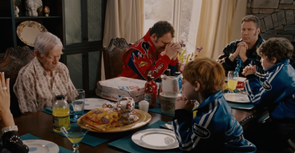 The family from movie "Talladega Nights" sits around a table of fast food praying over their meal.