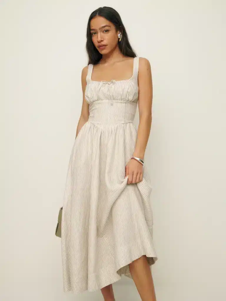 Model wearing a cream linen mid length dress.