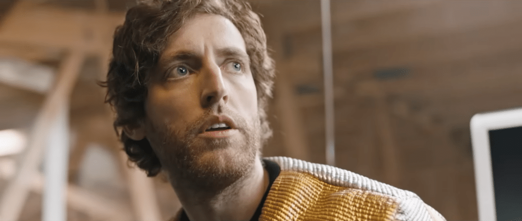 A man looking up, concerned. He has ginger hair and blue eyes. He is wearing a golden outfit.