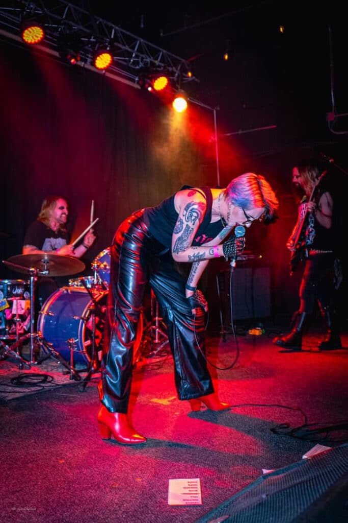 A musician singing into the mic, resting their hand on their knee bent at the waist.