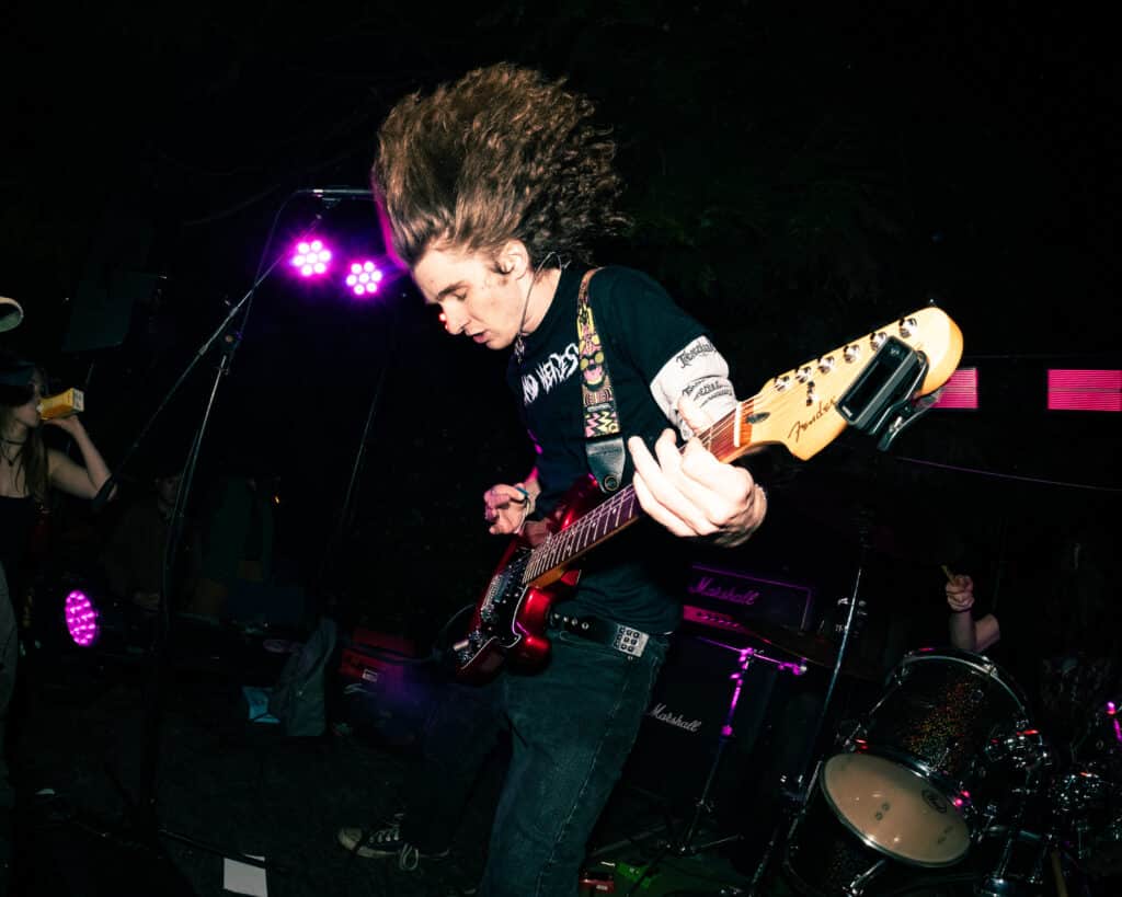 A punk musician headbangs and flips their hair while performing.