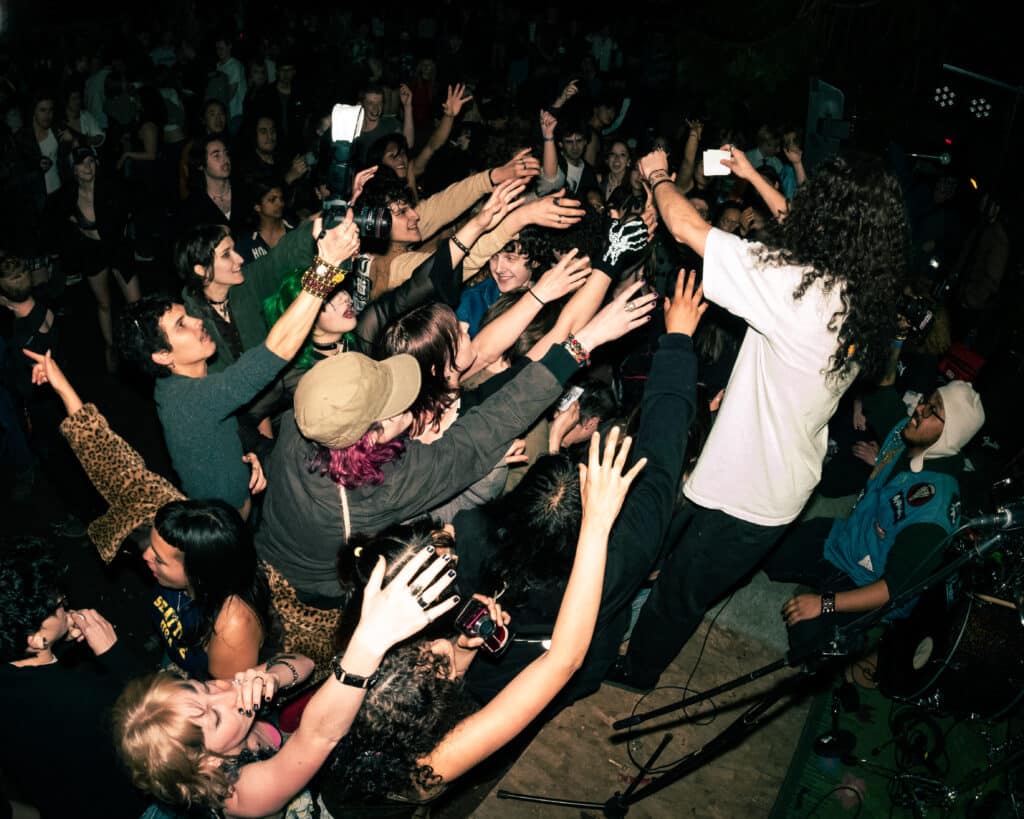 A wide-angle capture of a punk musician reaching out into the crowd.
