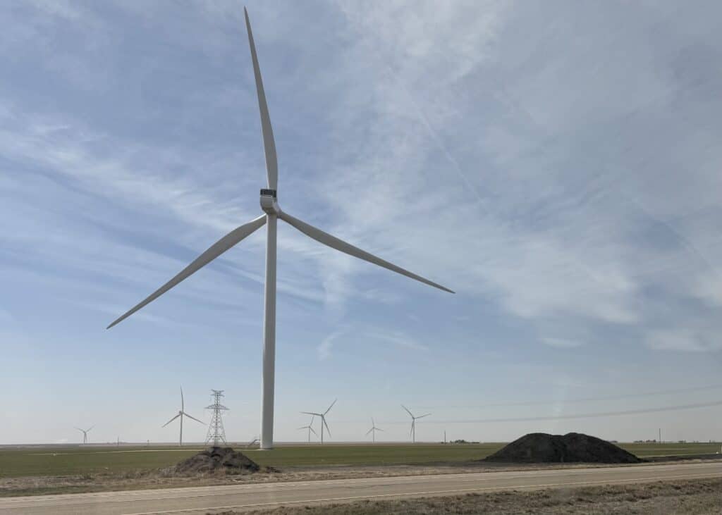 A landscape picture of numerous windmills on the side of the road for miles