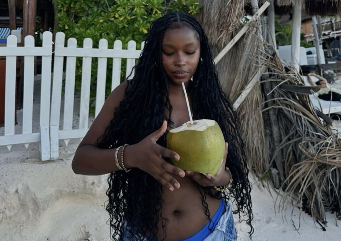 Girl in tropical setting with bohemian braids drinking from coconut.
