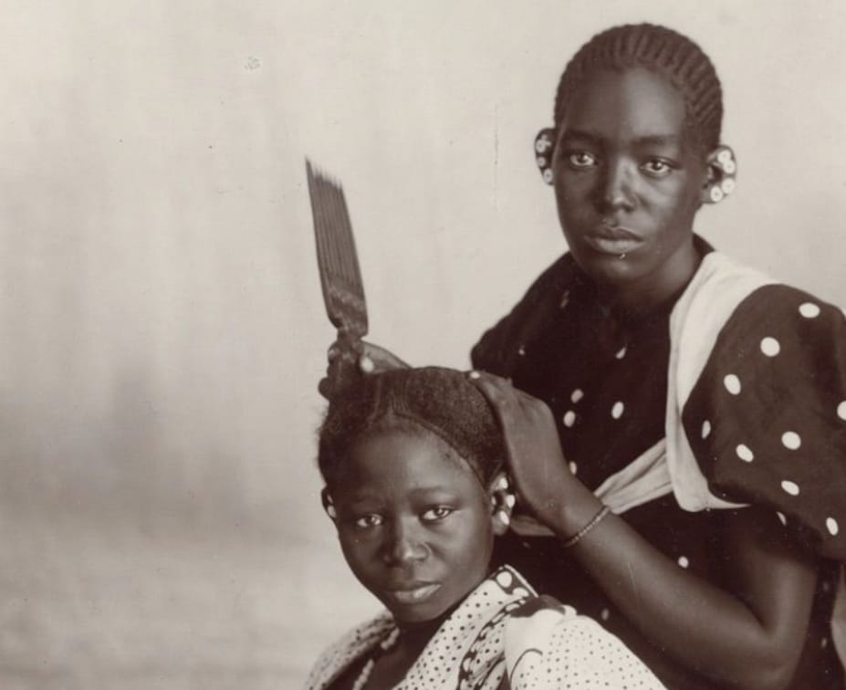 Old photograph of a woman doing a younger girl's braided hair.