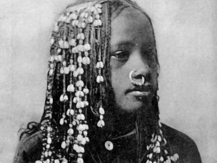 Older black and white photograph of a woman with a meticulously braided and beaded hairstyle.