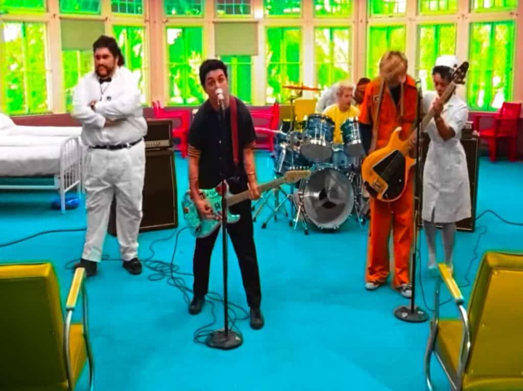 Green Day is performing in a mental hospital with nurses walking around them.