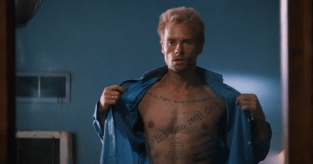 A man is staring at his tattoos in the mirror.