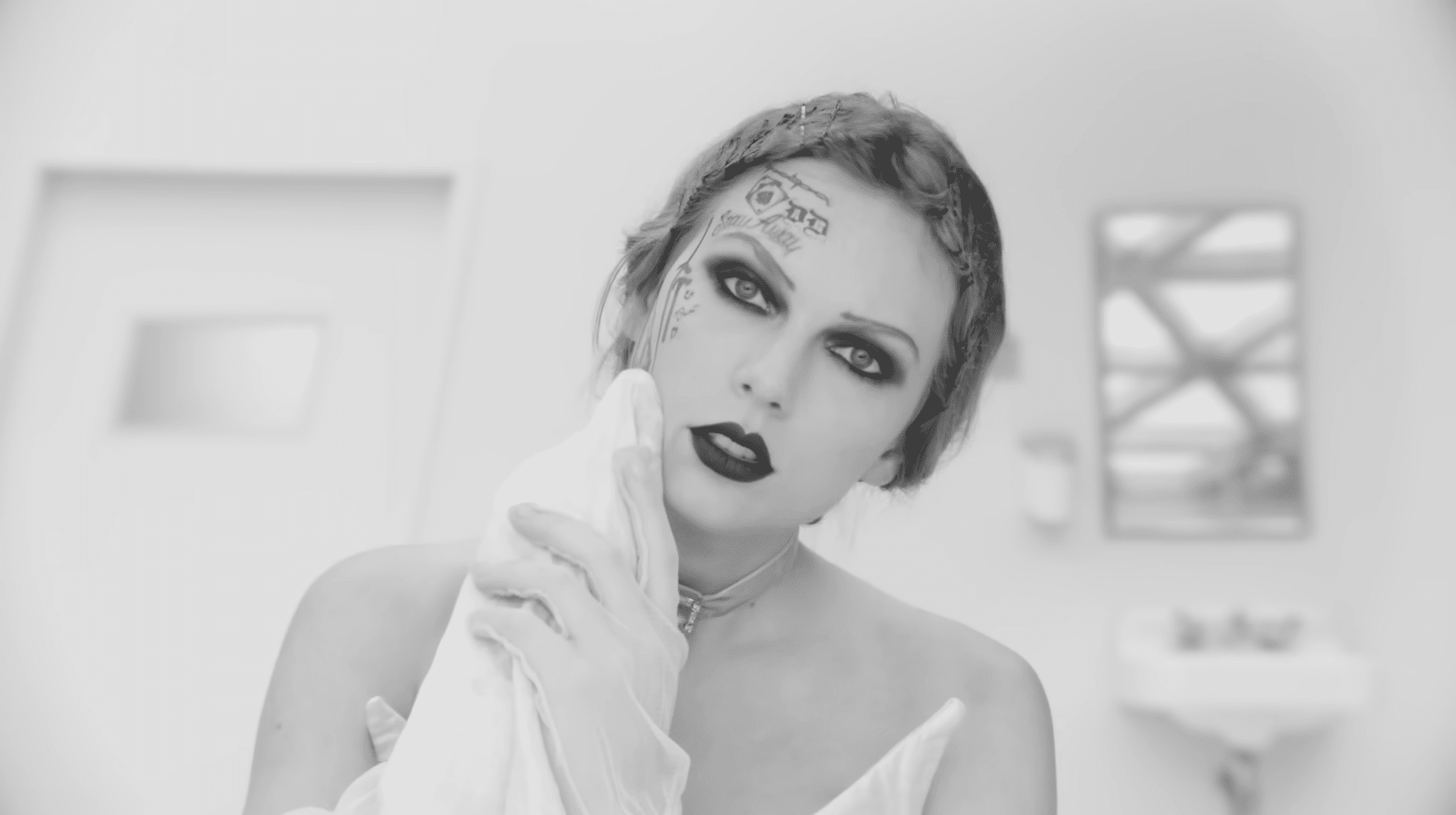 Taylor Swift in black and white in the music video for "Fortnight." She is seen wiping her face and revealing tattoos.
