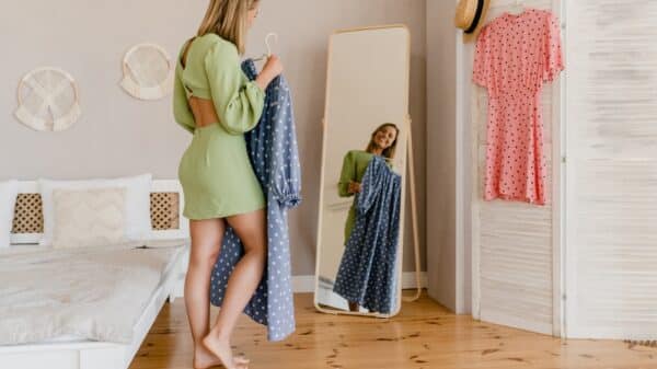 Woman in green dress standing in front of mirror holding blue dress.