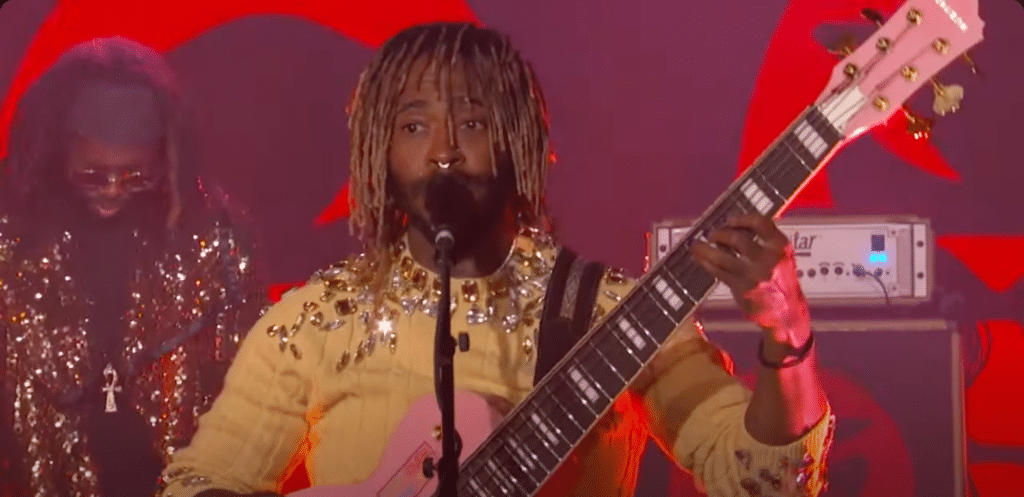 Artist Thundercat performing on stage singing "Black Qualls" and playing guitar.