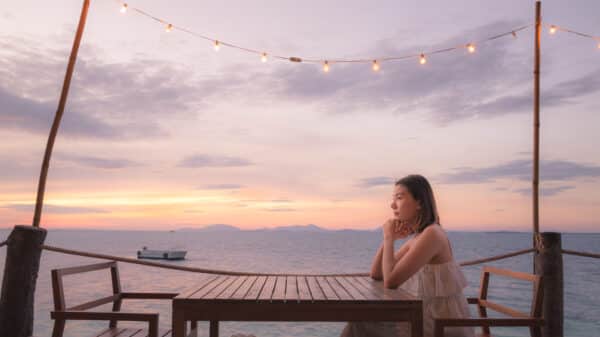 Woman sitting at table all alone with the sunset behind her.