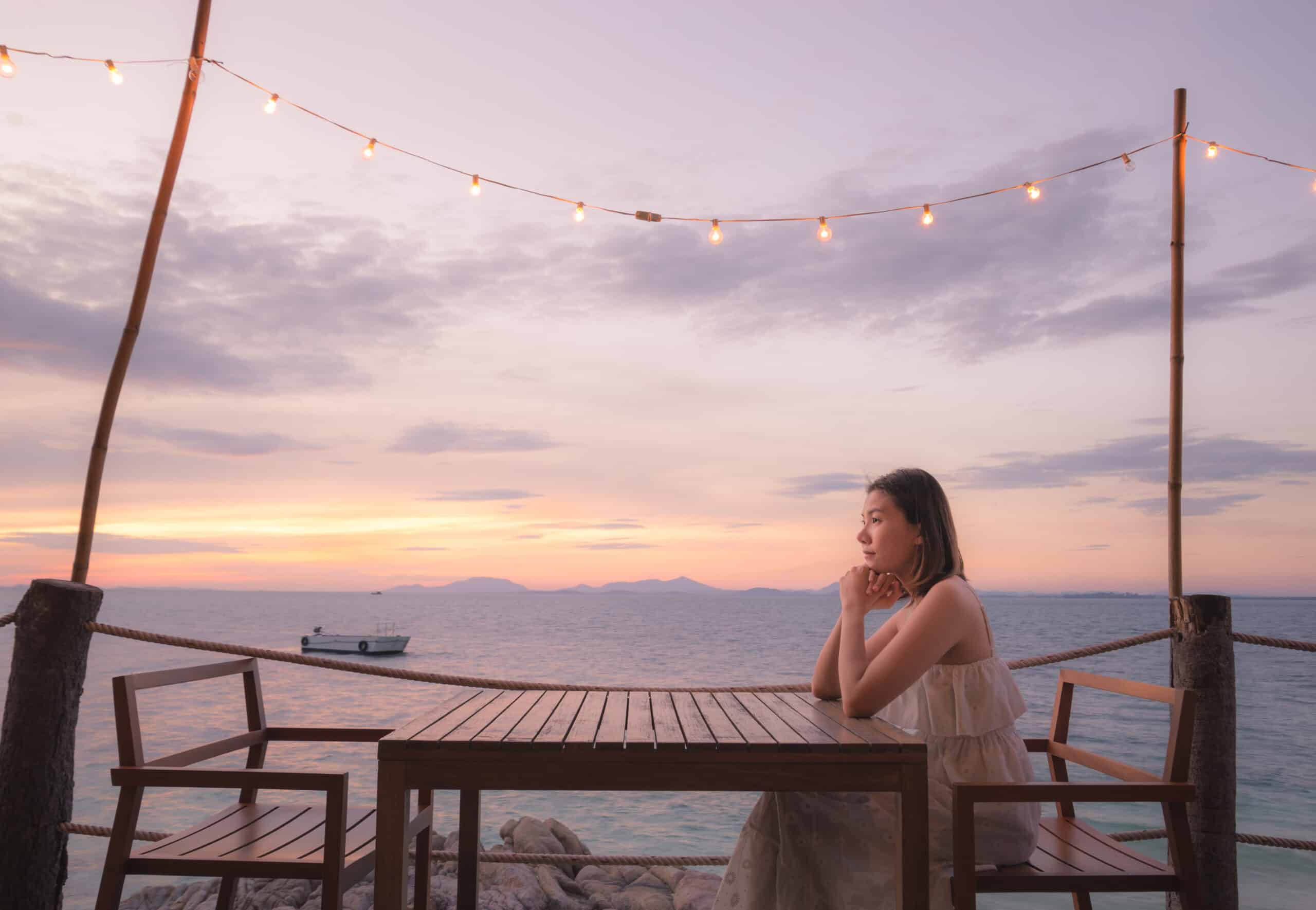 Woman sitting at table all alone with the sunset behind her.