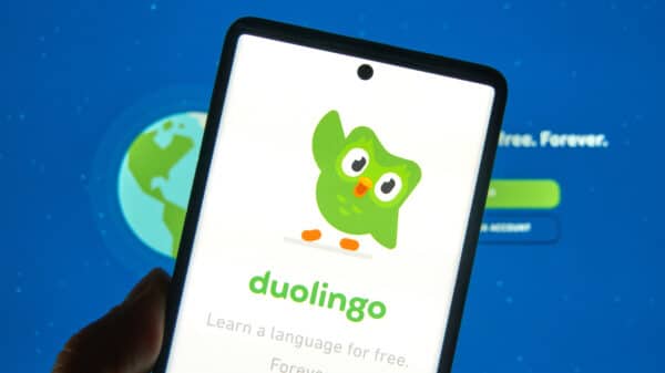 A phone is held up, showing the Duolingo mascot waving.