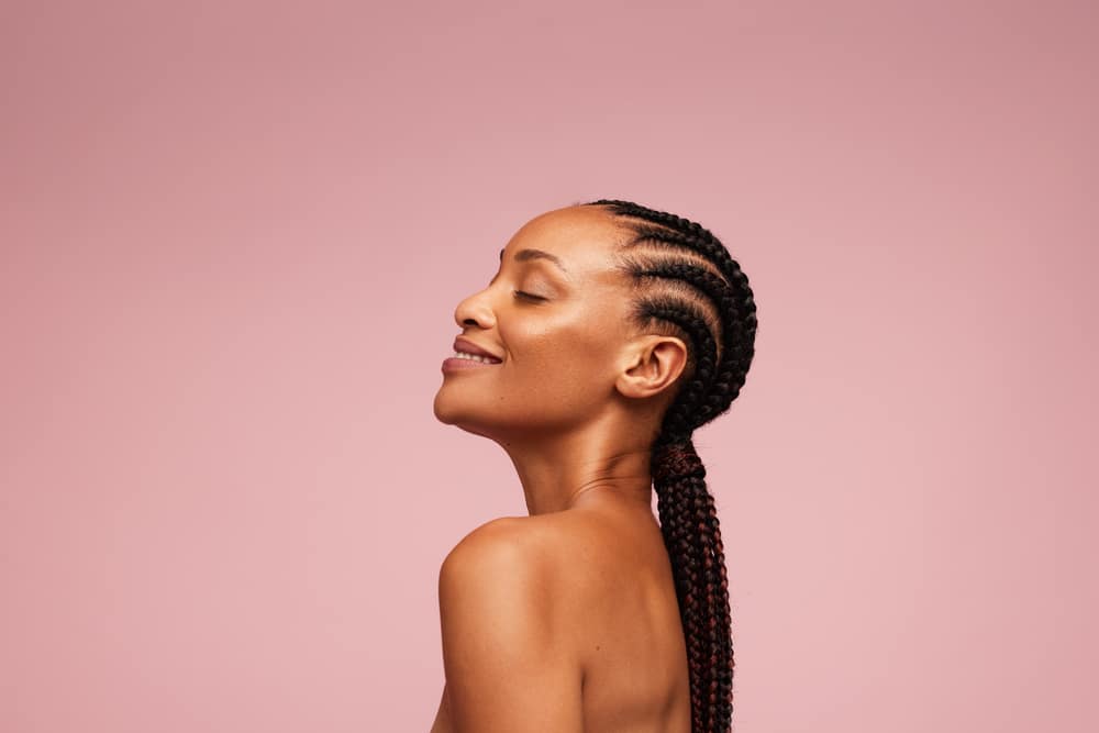 Side profile of women with straight back cornrows with a pink background.