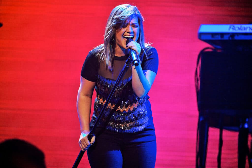 Kelly Clarkson holding a microphone and singing into it.