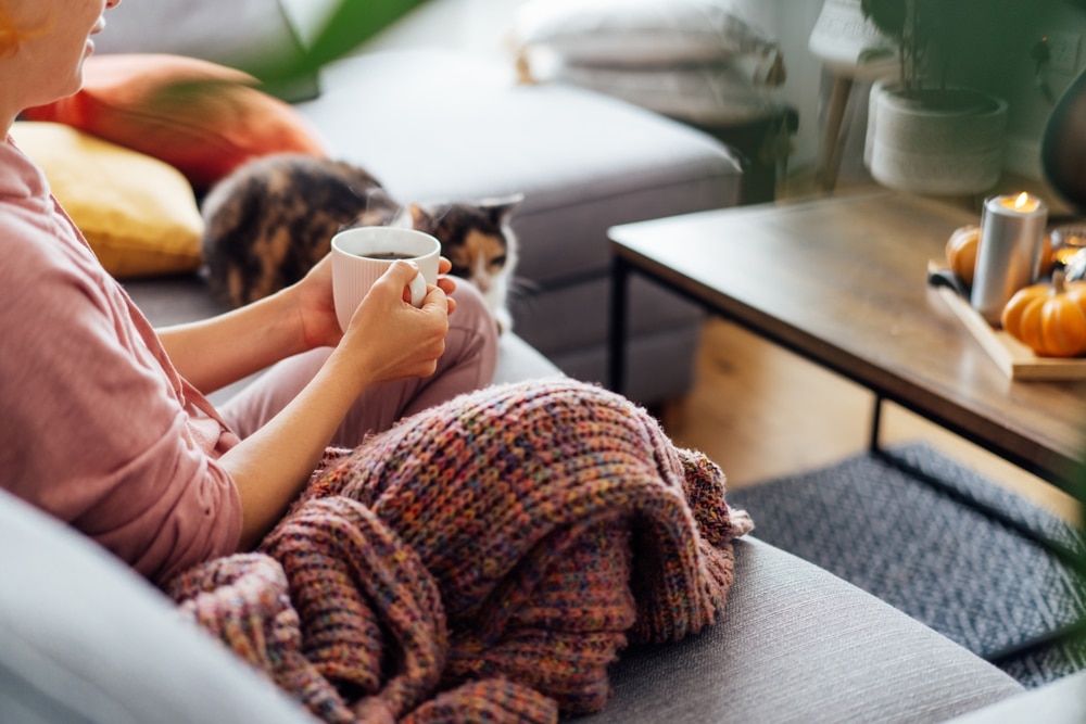 Photo of a woman practising self-care sat on her couch drinking a tea