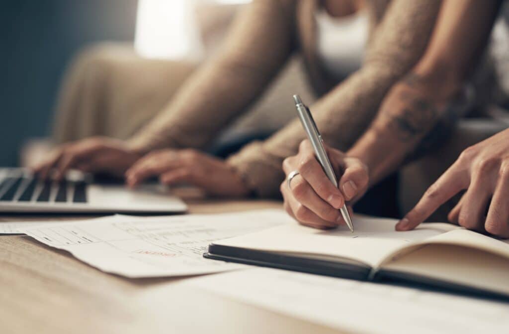 Person writing in a book and another typing