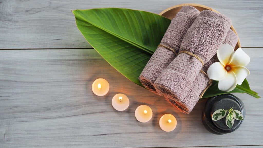 Photo of a selection of spa items laid out on a wooden board with flowers and candles light around