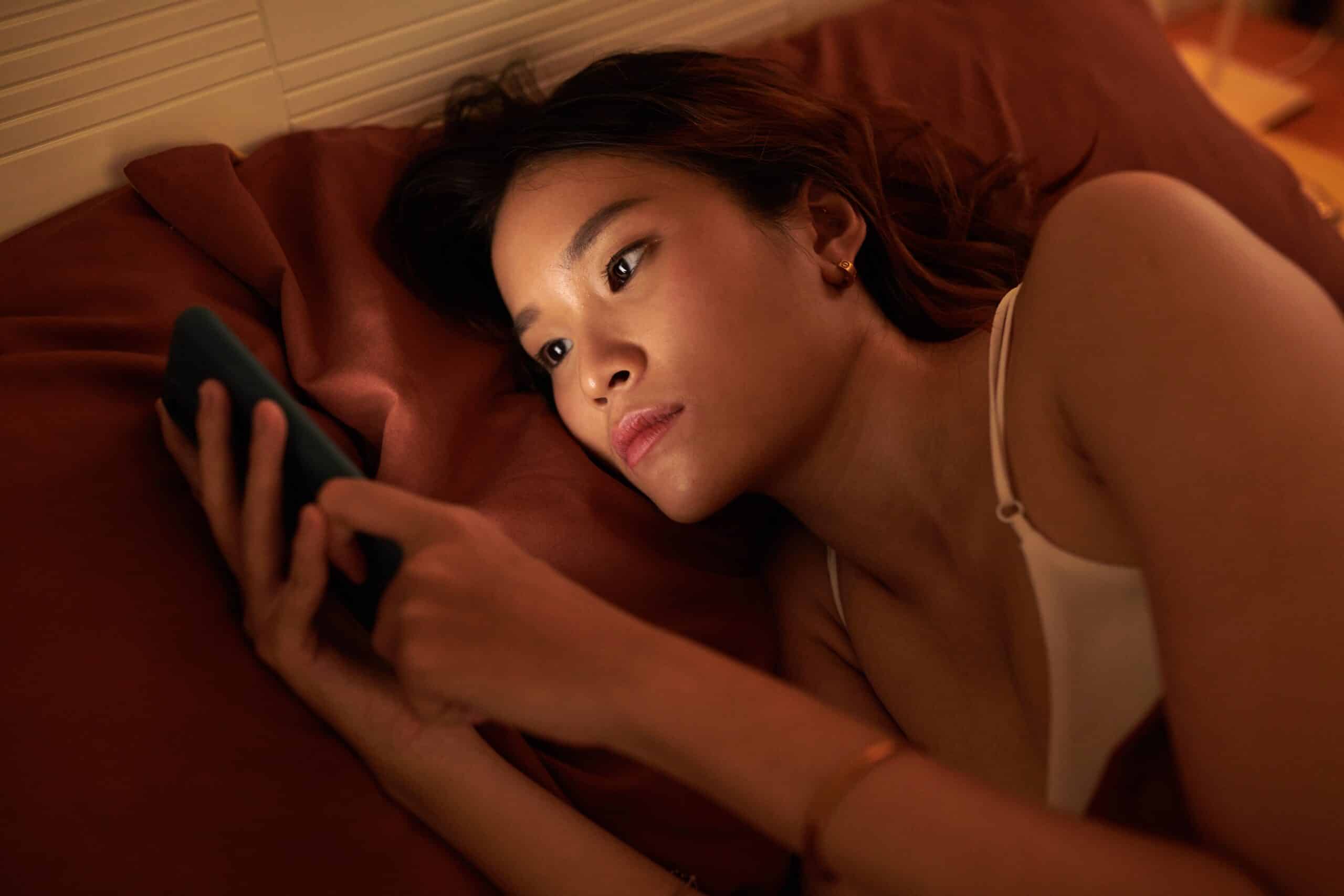 young woman scrolling on phone in bed