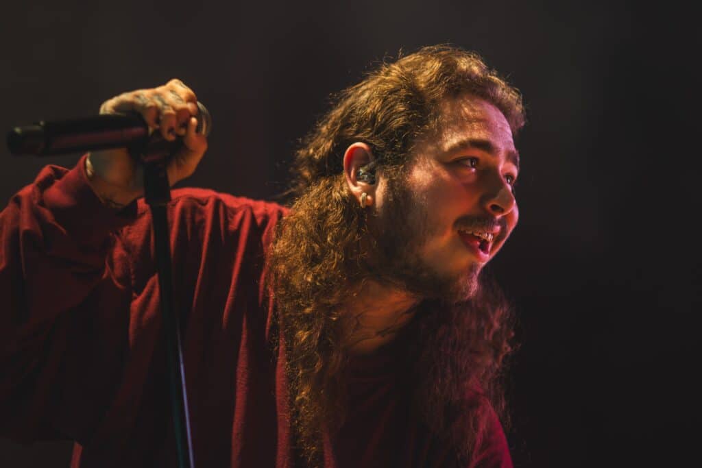 Post Malone crouched down while holding a microphone.