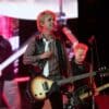 Green Day is playing on stage. Billie Joe Armstrong is in the center with Mike Dirnt to his right and Tré Cool on the screen to his left.