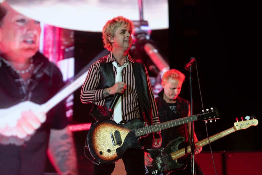 Green Day is playing on stage. Billie Joe Armstrong is in the center with Mike Dirnt to his right and Tré Cool on the screen to his left.