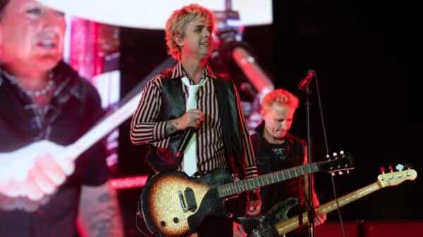 Green Day is playing on stage. Billie Joe Armstrong is in the center with Mike Dirnt to his right and Tré Cool on the screen to his left.