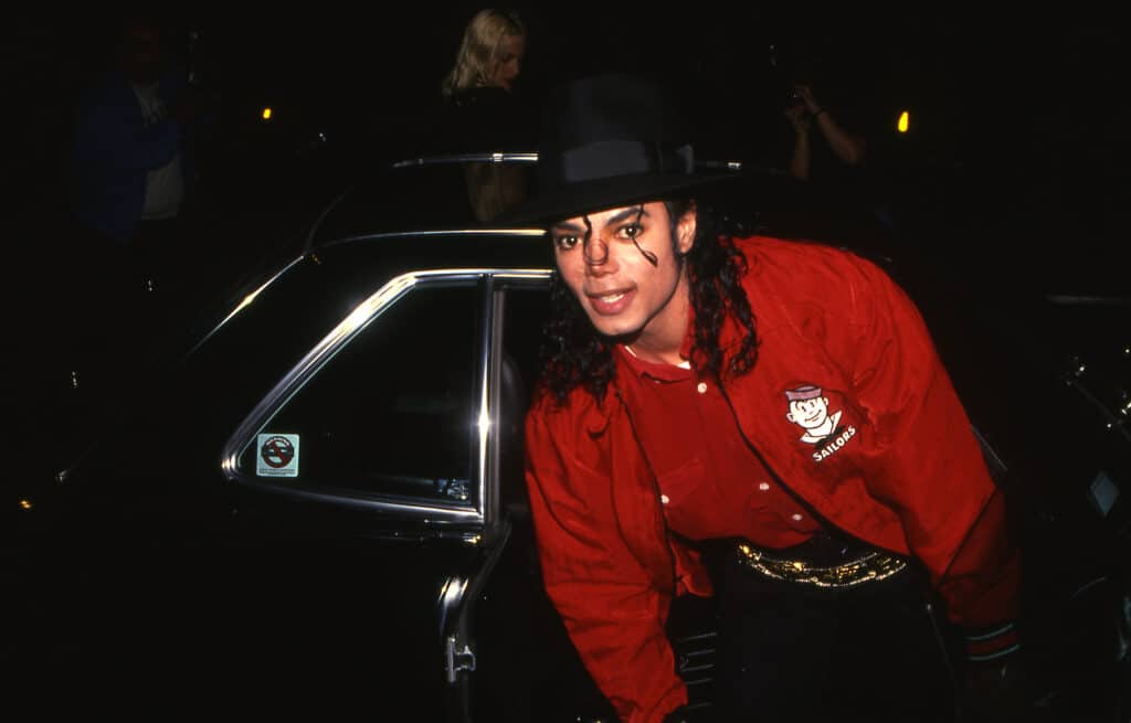 Michael Jackson standing in front of a car while wearing black and red.
