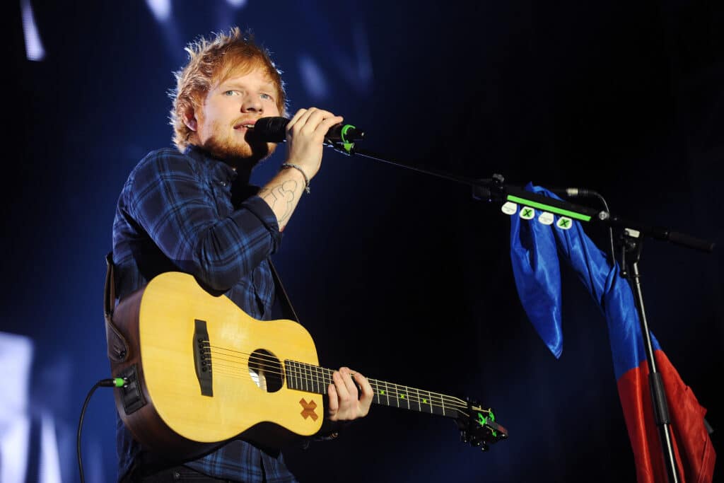 Ed Sheeran onstage holding a guitar and singing into a microphone.