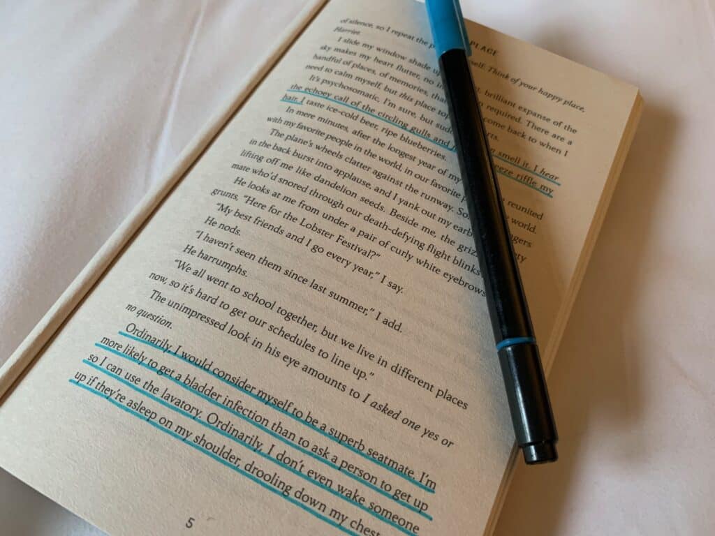 image of a loved book open with the first few pages bent behind it. the book is lying on a white sheet. some words have been underlined with the blue pen that is lying atop the book