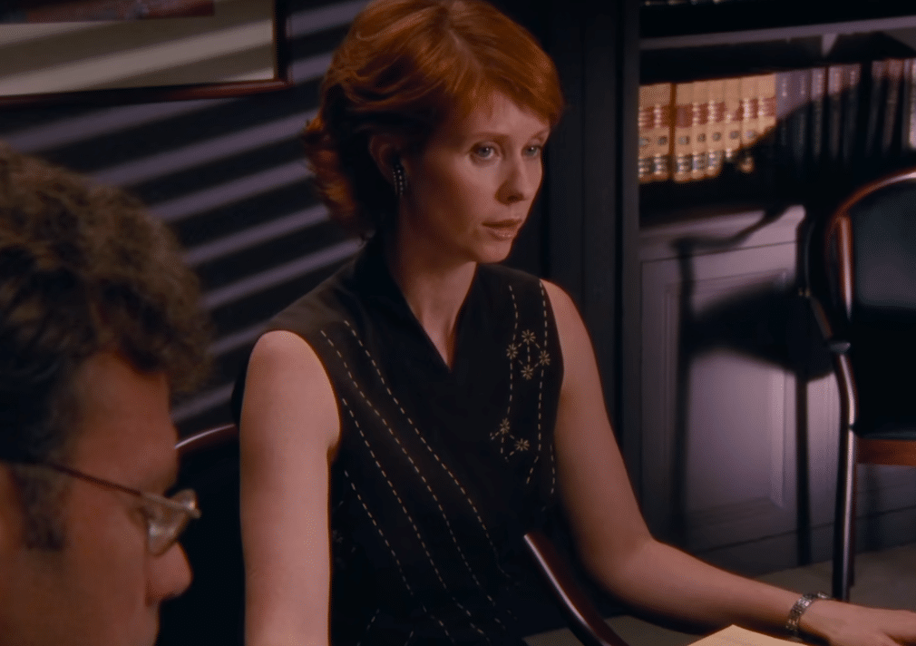 A still shot of Miranda from Sex and the City leading a meeting of lawyers, looking serious and focused.
