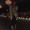 Runway model showcasing a black cape with chromed faux feather adornment.