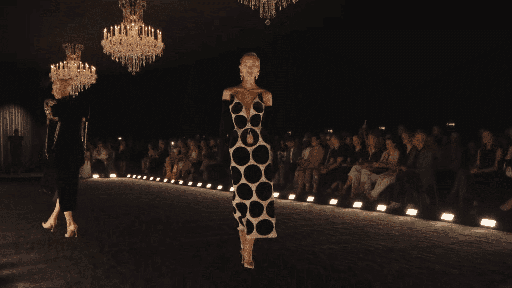 Runway model sporting a long 50's inspired polka dot dress with long black gloves and a vintage heel.