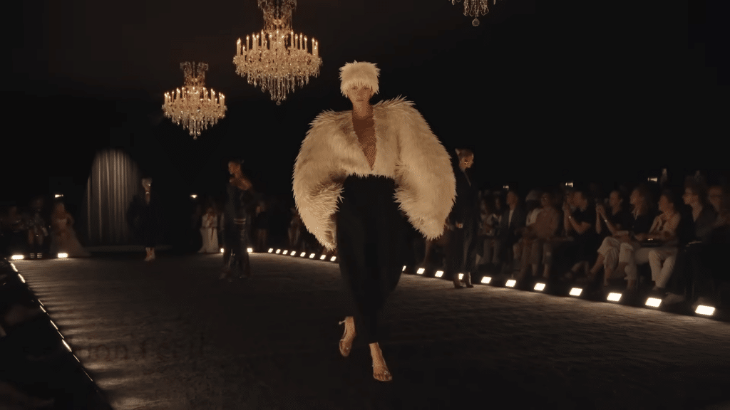 Runway model sporting a cream coat and had made of faux feather quills with black woolen pants.