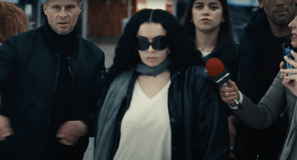 A screenshot of Charli XCX surrounded by paparazzi in the music video for "Von Dutch."