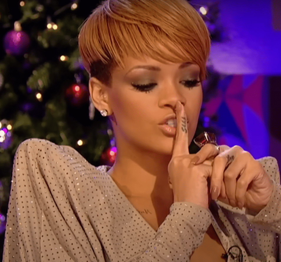 Rihanna showing off her "Shhh" tattoo on her finger by jokingly putting her finger to her lips.