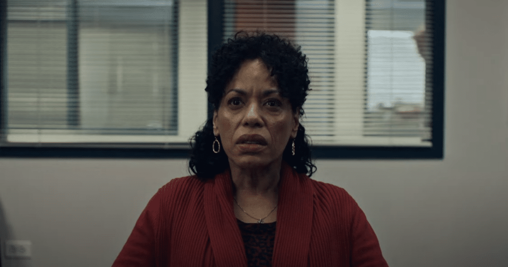 A woman with black curly hair, and gold hoop earrings stares straight ahead while looking disappointed.
