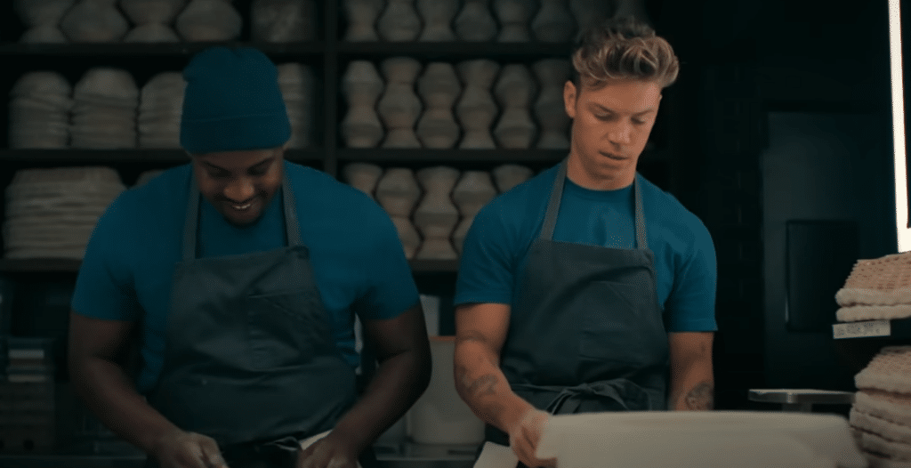 Two men in blue shirts standing in a kitchen, cooking.