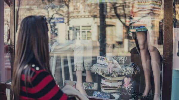 a woman longingly looking at fashion items through a store window