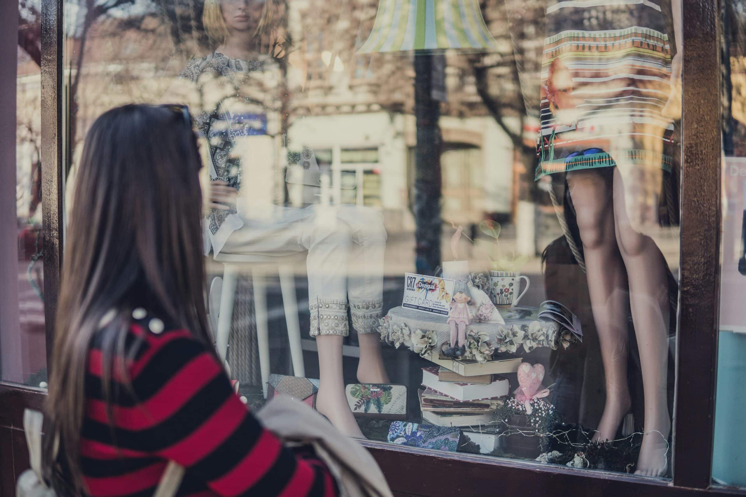 a woman longingly looking at fashion items through a store window