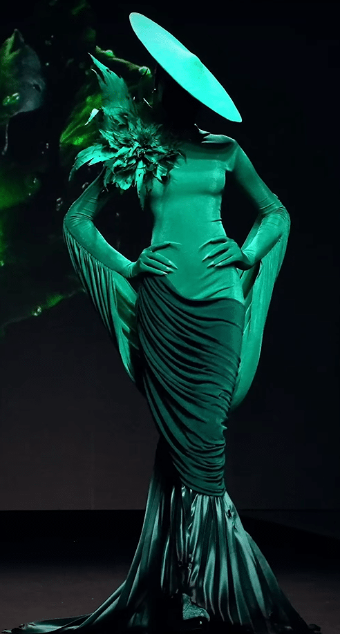 An emerald green dress and hat on a runway.