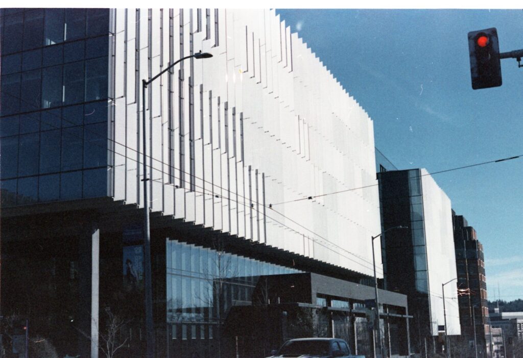 The broad side of a building. The top half is white and the bottom made of glass. The image has a strong blue/steel tone.