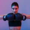 Image of young sports woman in tracksuit and black putting hands together in boxing gloves isolated over purple background
