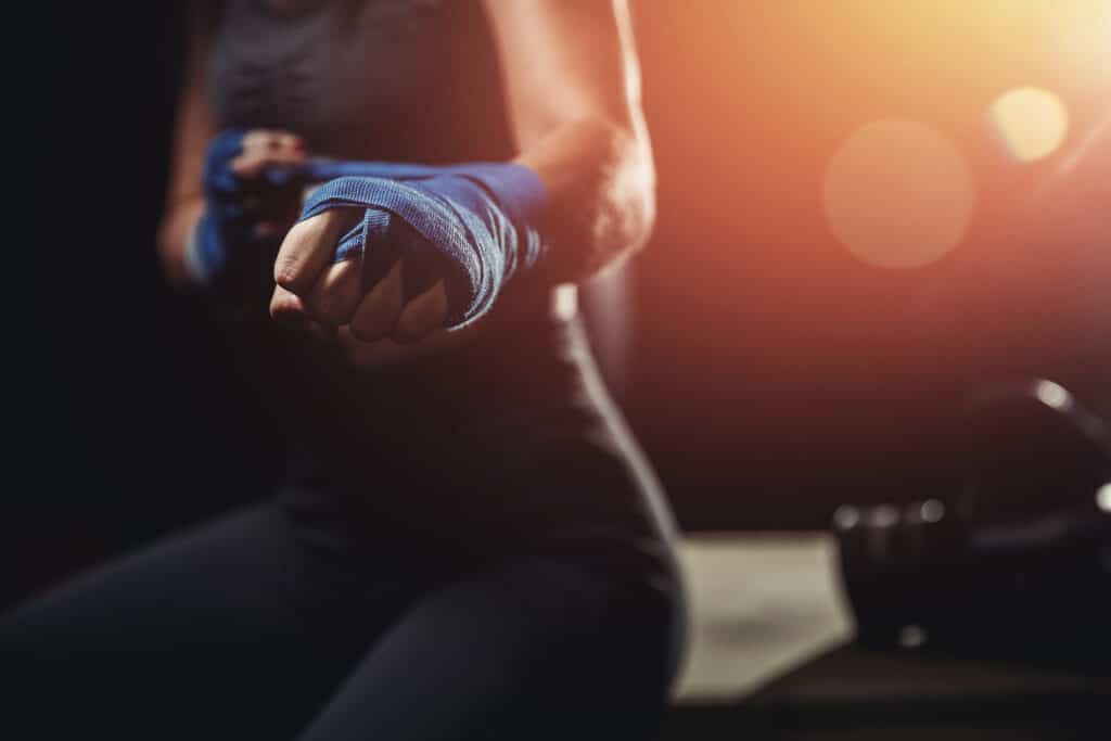 Woman wraps her fists in blue bandages for boxing gloves. Dark background.